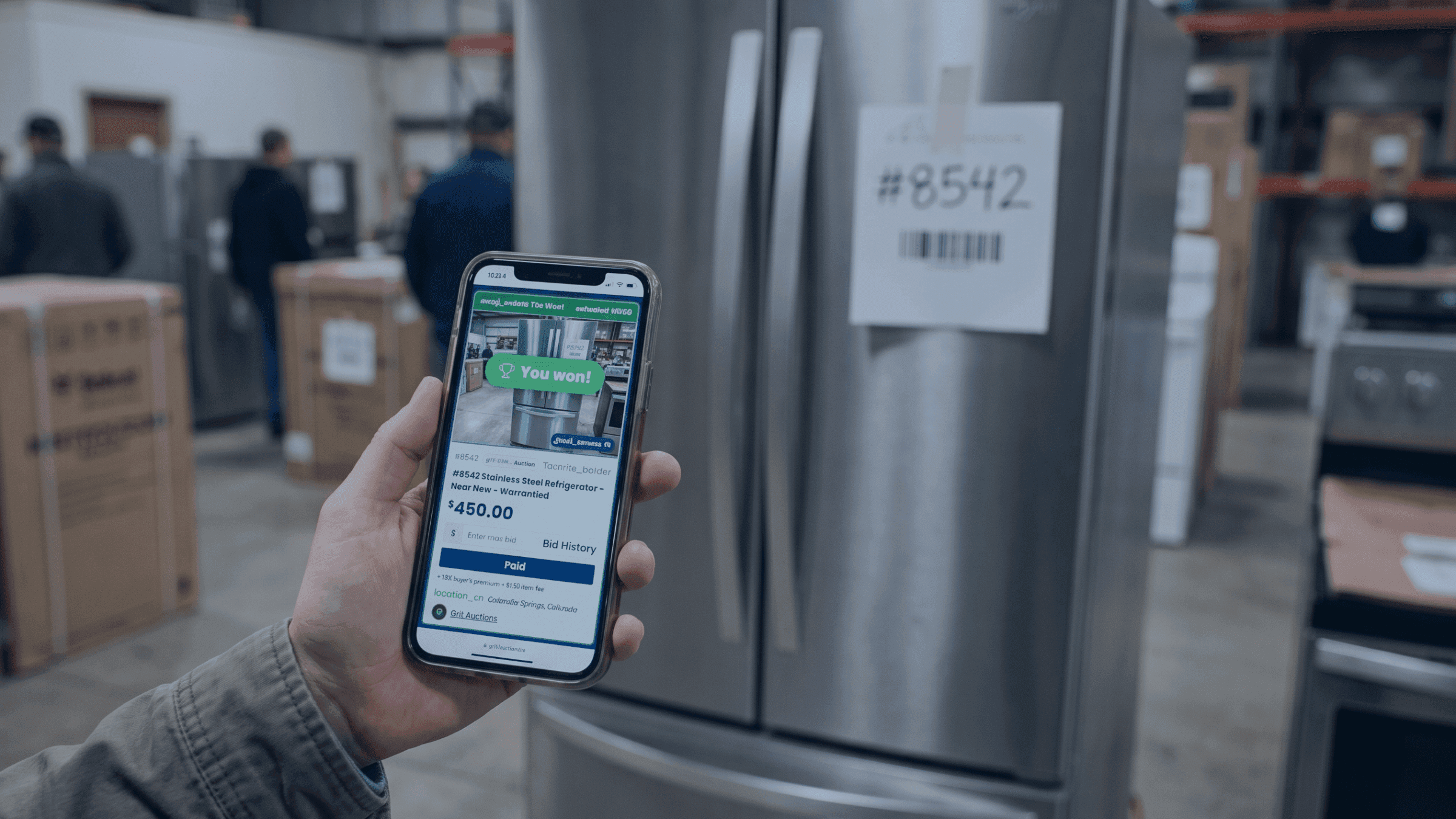 Person holding smartphone displaying appliance details next to a stainless steel refrigerator.